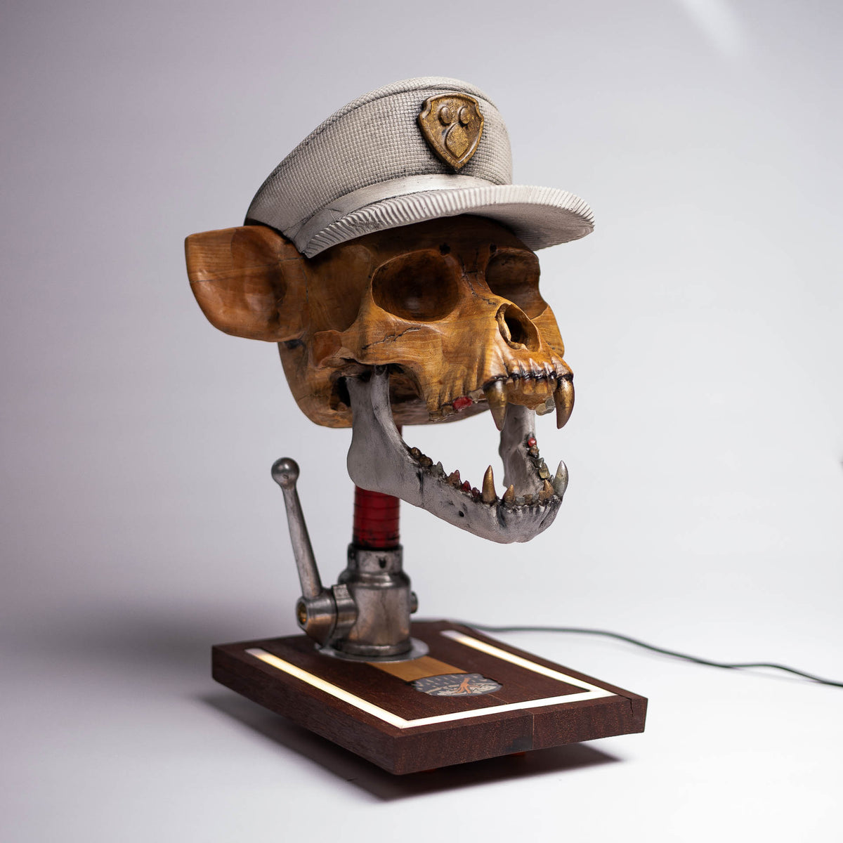Dead Chase sculpture: carved ash-wood skull with a concrete cap on a fire hose nozzle, seen from above at an angle