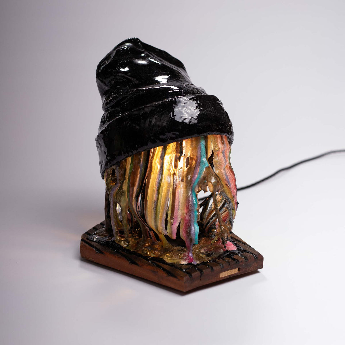 Melting Sahne sculpture: black winter hat above dripping multicolored epoxy resin on a wooden base